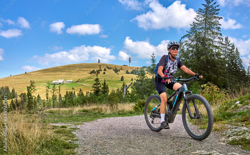 nice senior woman on her electric mountain bike cycling on Feldberg summit, top of German Black forest