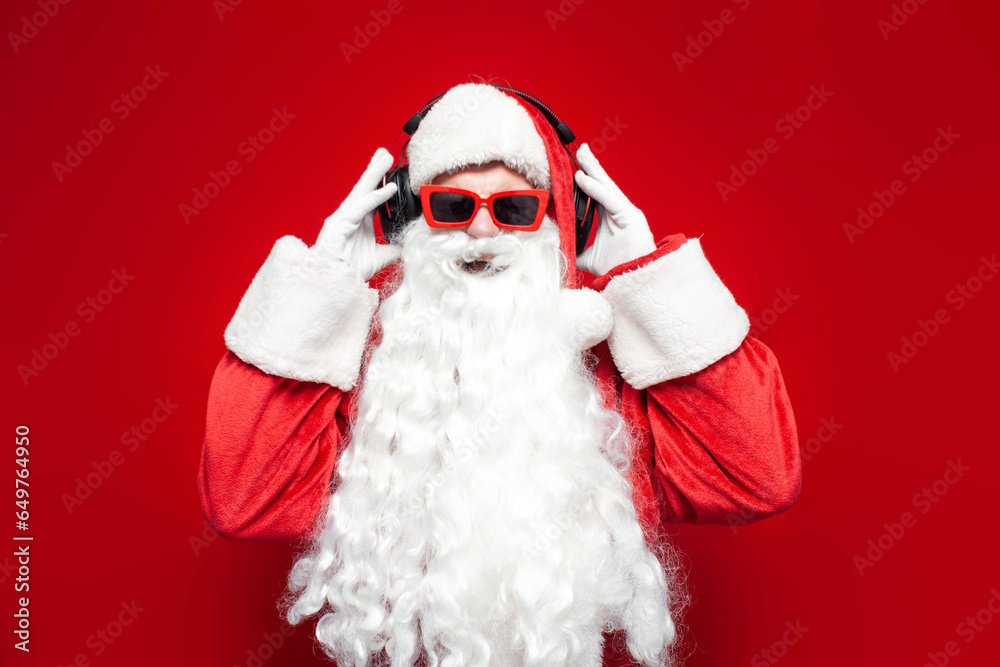 Φωτογραφία santa claus in hat and glasses listens to music in headphones and sings on red b