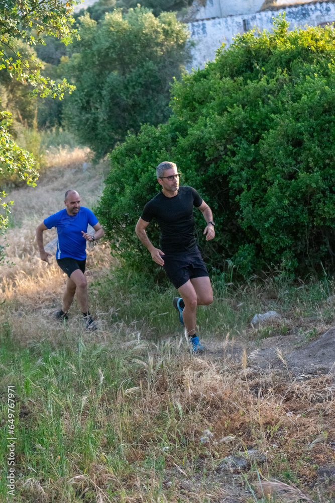 Two trail runners, one bald, the other with gray hair, conquering rugged paths together. A dynamic duo in nature's embrace.