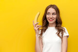young pensive girl holding banana and smiling on yellow isolated background, woman dreams and sexualizes the fruit