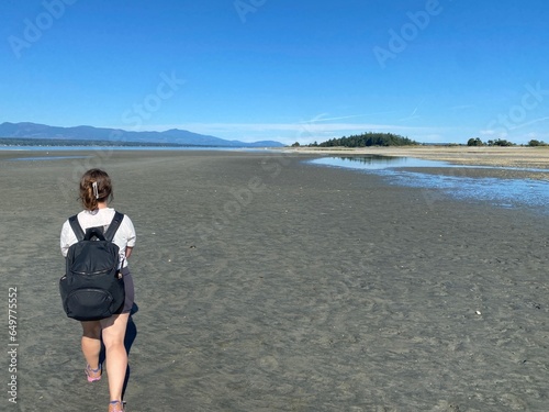 A young woman hiking alone at low tide between Denman Island and Jáji7em and Kw’ulh Marine Park, where the two islands connect, on a beautiful sunny day in the Gulf Islands, Canada.