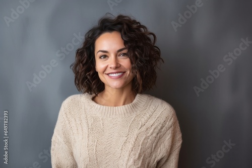Obraz na płótnie Cheerful woman with curly hair and a joyful smile wearing a grey sweater in a studio portrait. w salonie