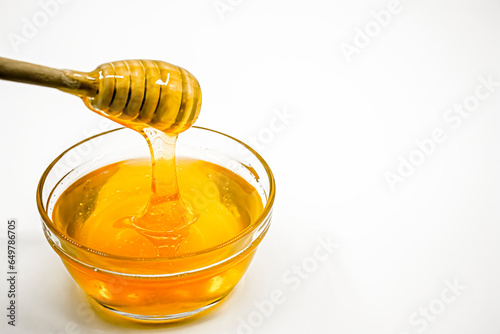 Honey flows from the honey spoon into the glass bowl full of honey. Photograph.