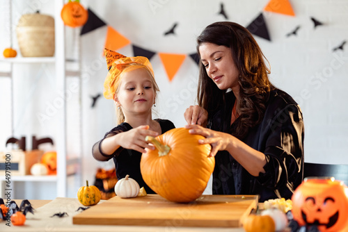 Mother and daughter carving pumpkin for Halloween autumn holidays. Mother and daughter in costumes decorating the home and having fun.