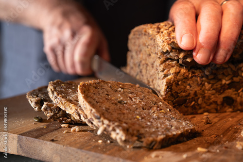 Cutting fresh whole wheat bread into slices on a wooden work surface. Close-up. photo