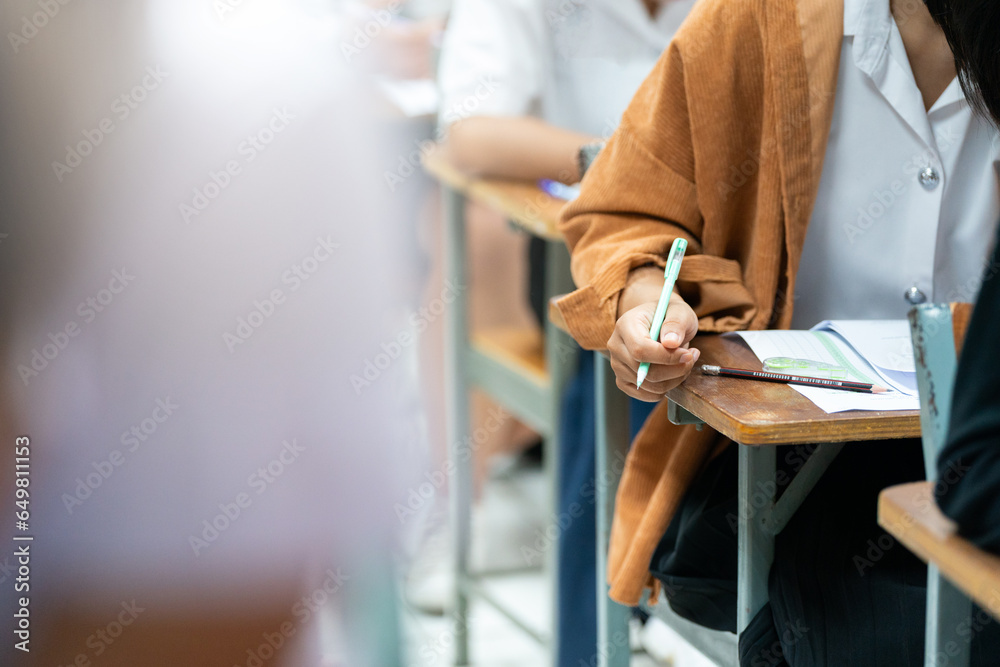 Close-up of a student's hand writing on paper taking educational admission test in university classroom - obrazy, fototapety, plakaty 