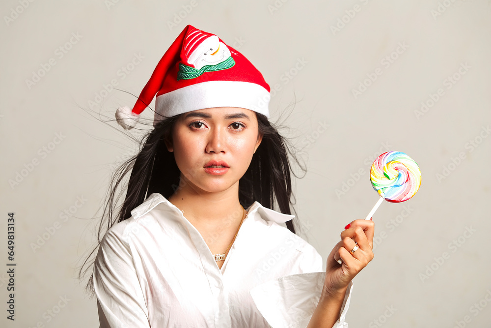 Beautiful young Asian woman wearing christmas hat and white dress holding lollipop candy isolated on white background. christmas concept. Beautiful young Asian woman wearing christmas hat and white dress holding lollipop candy isolated on white background. christmas concept.