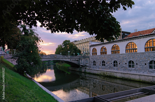 Morning landscape view of Ljubljana. Embankment of Ljubljanica River with illuminated colorful historic houses and famous Dragon bridge (Zmajski most) in the background. Tavel and tourism concept photo