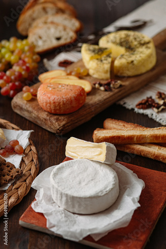 Variety of delicious dishes on a wooden table. The focus is on the round wheel of white cheese in the center. 3 types of cheese, grapes, bread, crackers on a wooden table. medium shot, vertical frame