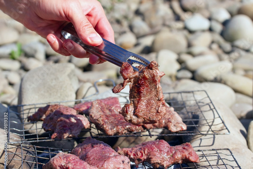 A man turns over pieces of meat, beef on a barbicue grill on a summer beach. photo