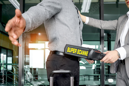 Security man holding metal weapon detector scanner for checking male passenger who going through procedure of physical inspection at entrance airplane gate. Airport security check before flight.