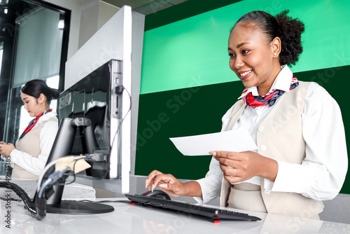 Happy Africa female passenger service agent with curly hair holding boarding pass ticket, checking information on computer at check in area airport terminal, traveling trip airplane transportation.