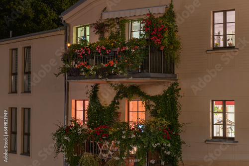 old house at night with light in the windows  balconies decorated with flowers and plants.