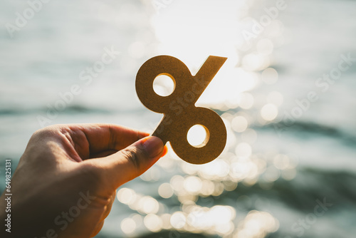 Businessman's hand holding a symbol Percentage with blur sea background, concept of systems of raising or lowering Fed interest rates to correct inflation concepts.