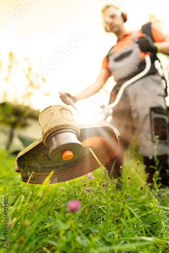 Close up of man using grass trimmer for cutting lawn in his garden on sunny summer day.