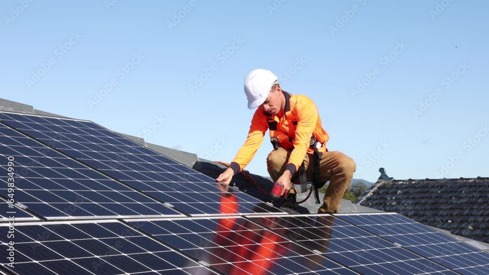 Solar panel technician with drill installing solar panels on house roof on a sunny day.