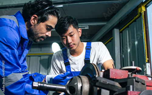 Two adult handsome male mechanics wearing uniform, using machine for fix, repair car or automobile components, teamwork helping, working in car maintenance service center or shop. Industry Concept.