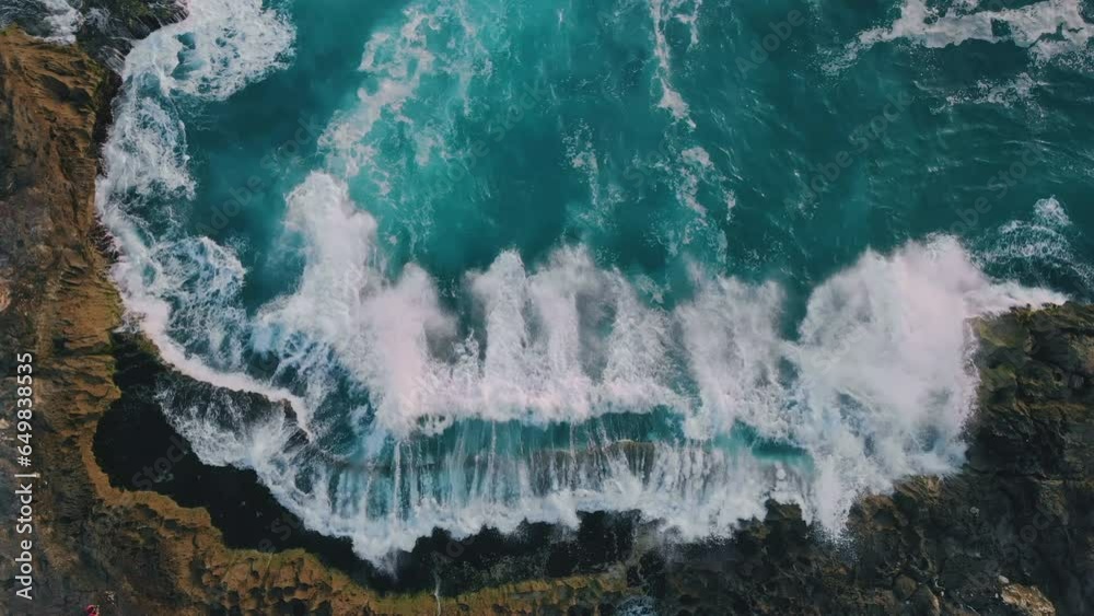 Top down aerial view from above of giant ocean waves crashing and foaming on empty sand tropical beach with big rock stones. Bird's eye aerial shot of golden beach meeting deep blue ocean water.