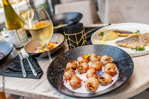 Cooked grape snails in shells on a table in a restaurant with a glass of white wine