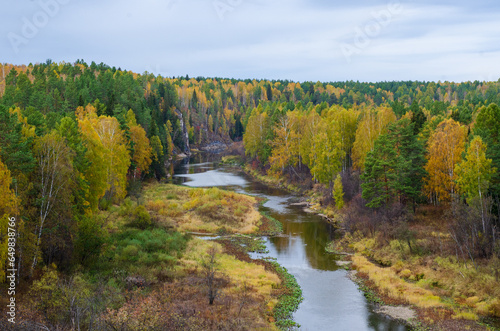 A calm river meanders through a colorful autumn forest. Aerial view of fall forest and river. Beautiful autumn landscape.