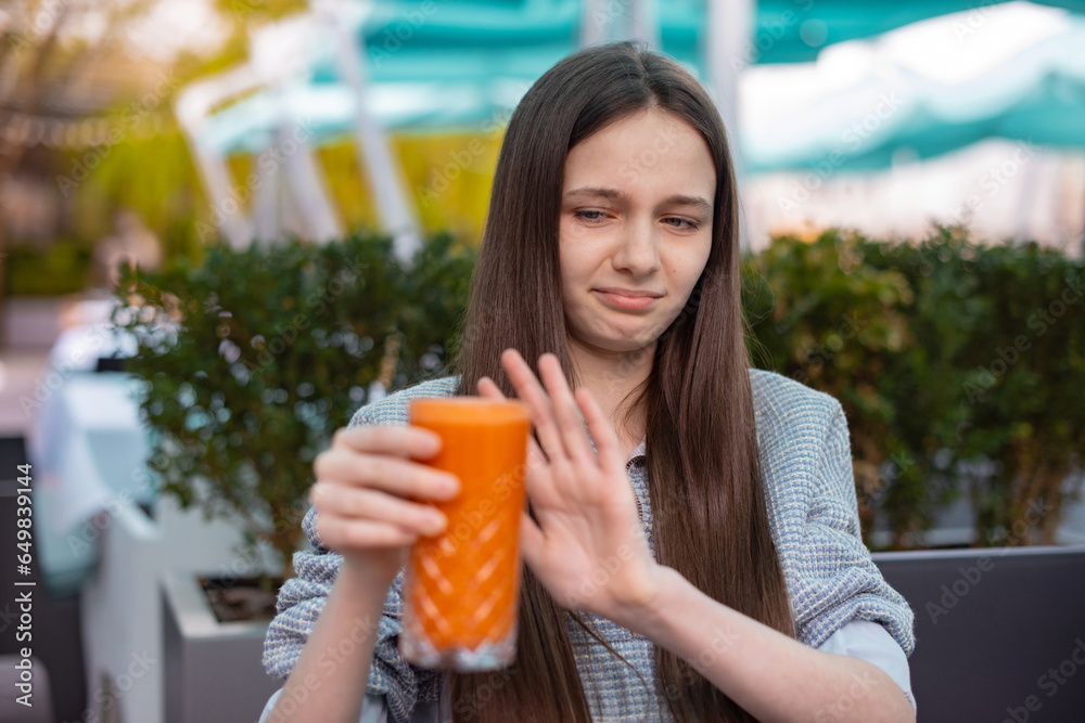 girl refuses to drink carrot fresh. teenager girl shows a sign of refusal of nutrition vegetarian drink girl refuses to drink carrot fresh. teenager girl shows a sign of refusal of nutrition vegetarian drink
