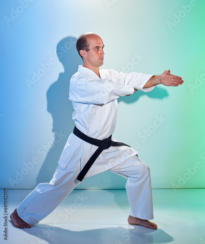 Adult man with black belt training formal exercises against color background with blue and green tint