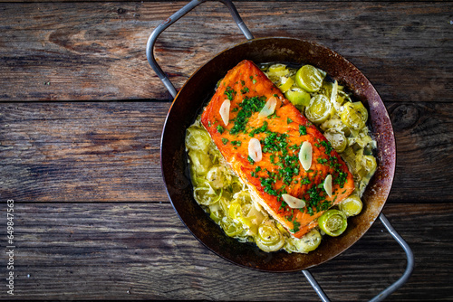 Fried salmon steak with cooked leek and garlic on frying pan on wooden table