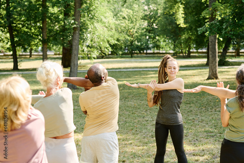 Young coach showing exercises to senior people during sport training in the park