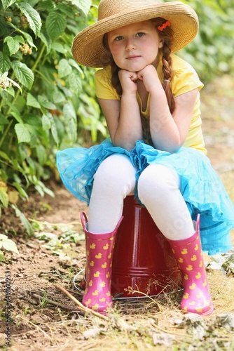 A Girl Wearing A Straw Hat And Sitting On A Large, Red Pail; Troutdale, Oregon, United States Of America photo