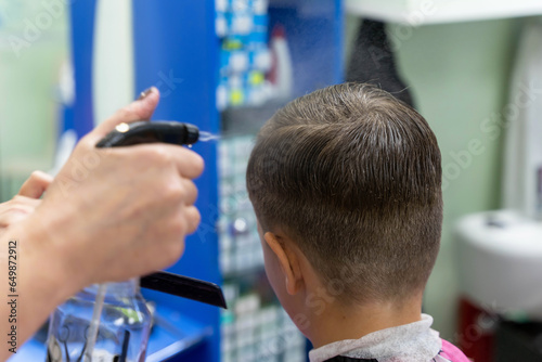  hairdresser sprays a child's hair with a spray gun during a haircut 