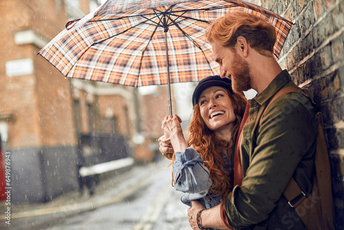Young redhead couple using a umbrella to avoid the rain while on a date in London UK photo