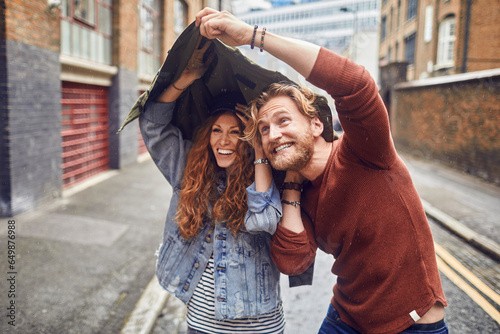Young redhead couple using a jacket to avoid the rain while on a date in London UK