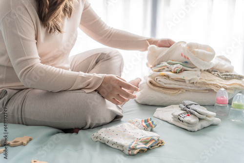 Pregnant asian woman getting ready for the maternity hospital preparing and planning baby clothes for new baby of pregnancy packing baby stuff on bed photo