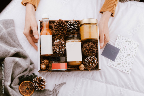 Manos ofreciendo una caja de regalos conteniendo productos alimentarios a la ocasion de Navidad.