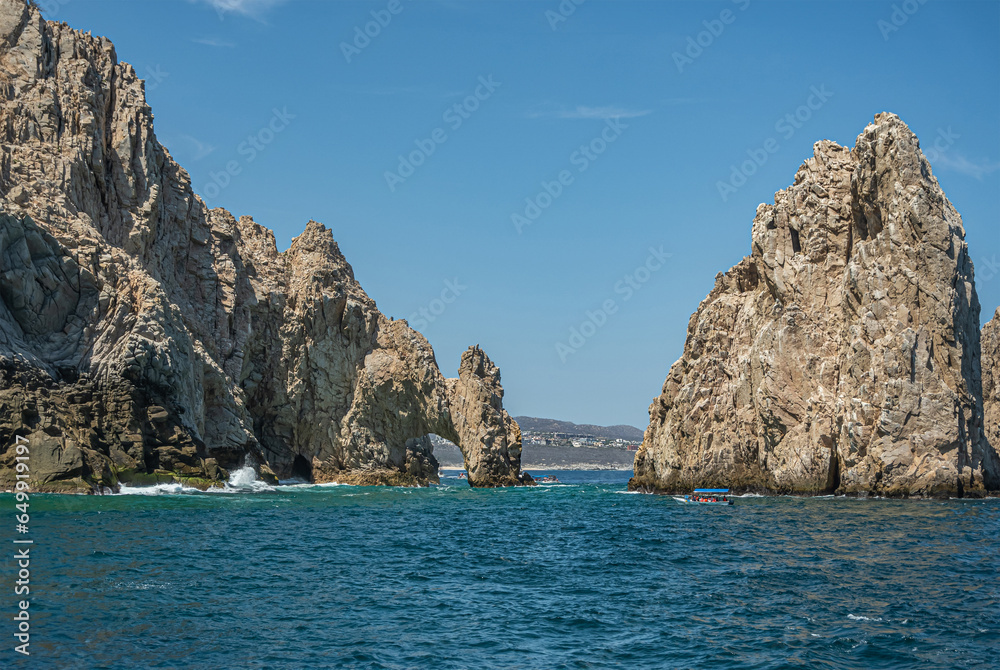 Mexico, Cabo San Lucas - July 16, 2023: South view on Reserva de Los Marina, El Arco and channel between tall gray boulders in greenish ocean water. Cityscape and beach on horizon