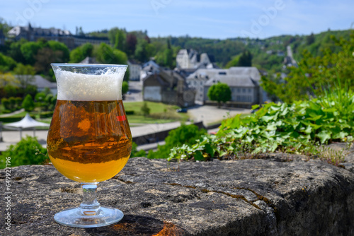 Glass of blond strong Belgian abbey beer on old castle wall in sunny day with nice view on old town Bouillon, Belgium photo