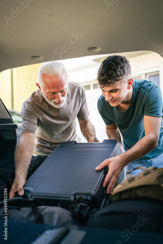 Two men Teenager and senior grandfather pack baggage in trunk of car