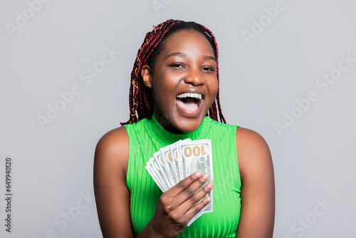 Happy smiley delighted African American dark skinned woman with braids smiling holding dollars bunch of money in hands showing at camera celebrating photo