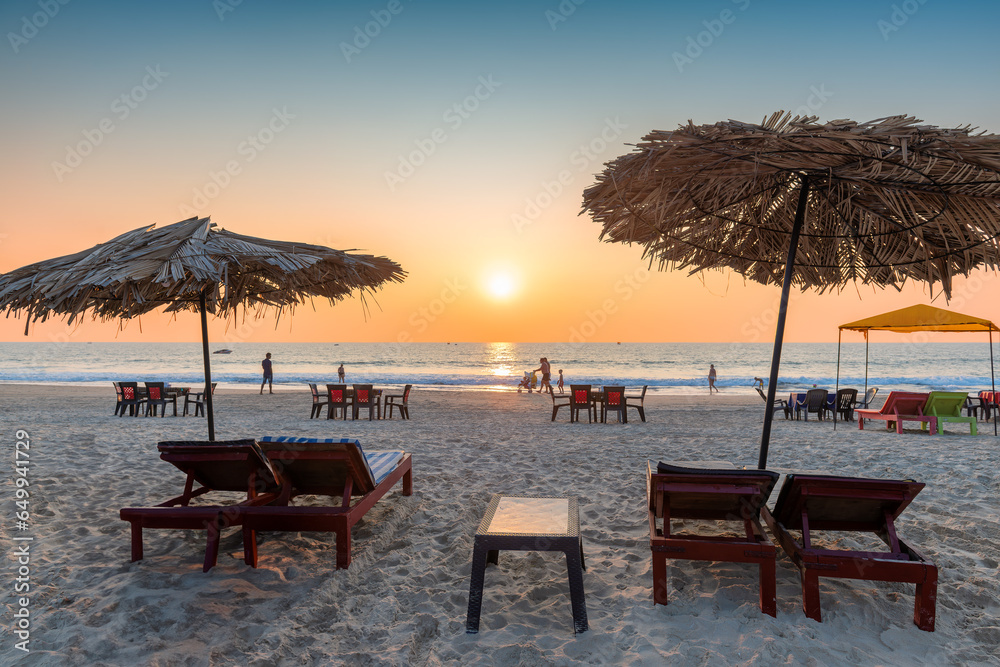 Tropical sunny beach party at Sunset with Sun umbrellas and lounge chairs in GOA, India.