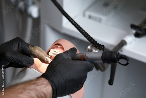 Close-up of dentist hands who is learning to treat teeth on human head mannequin. Hands of male medical student in black sterile gloves holding a dental drill. Stomatology and orthodontics concept.