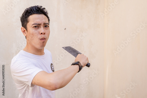 Indonesian men ready pose when hold the butcher knife wear white tshirt. The photo is suitable to use for man expression advertising and fashion life style. photo
