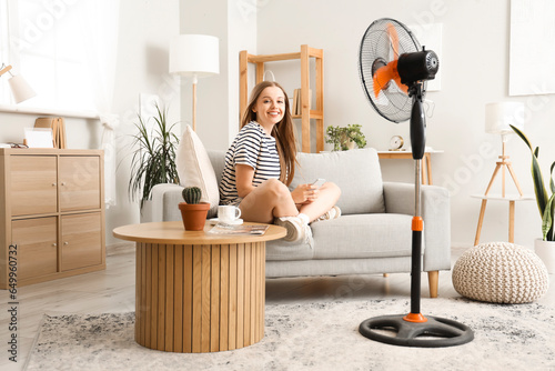Cuadro en lienzo Young woman with mobile phone and blowing electric fan at home