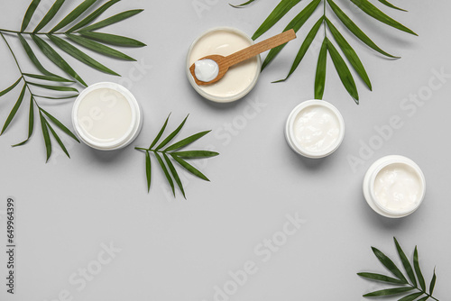 Composition with jars of cosmetic products and palm leaves on grey background