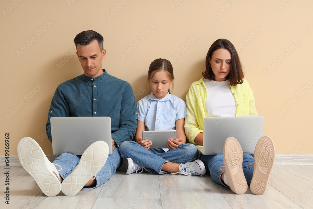 Family involved with gadgets sitting near beige wall Family involved with gadgets sitting near beige wall