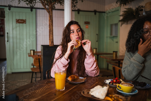 Young woman having brunch with her friends on sunday. She is eating a salmon bagel sandwich.