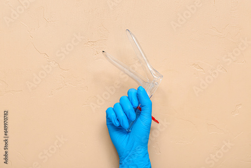 Hand in medical glove and with gynecological speculum on beige background photo