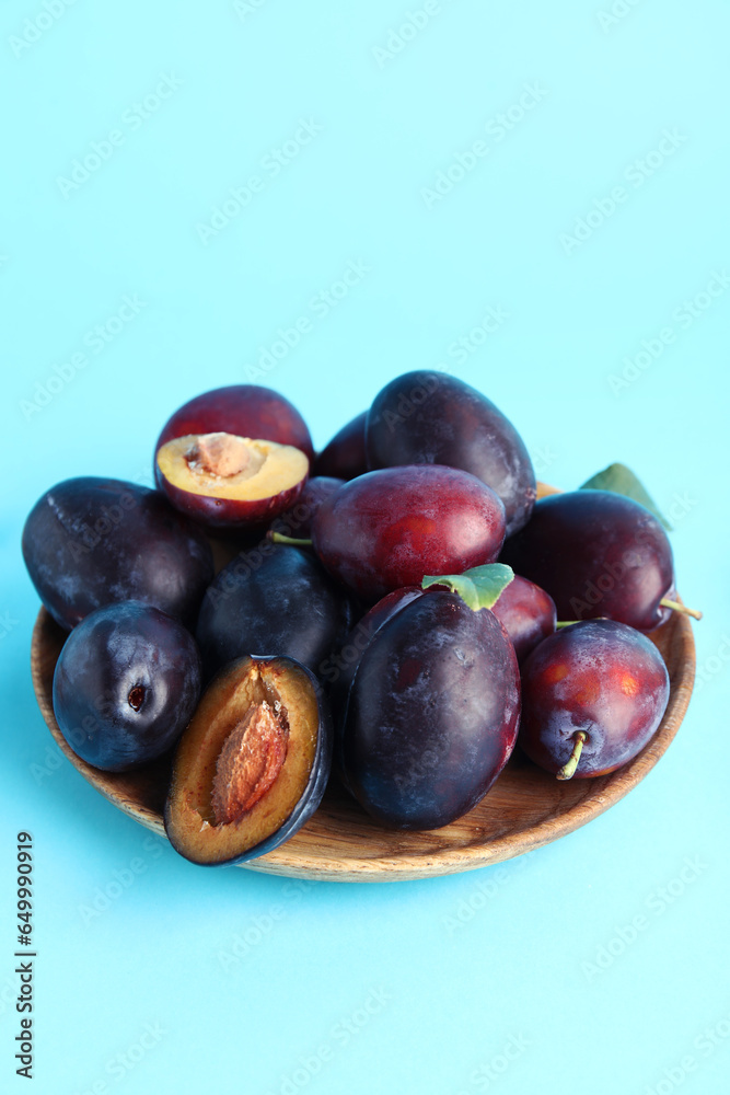 Wooden plate with fresh ripe plums on blue background