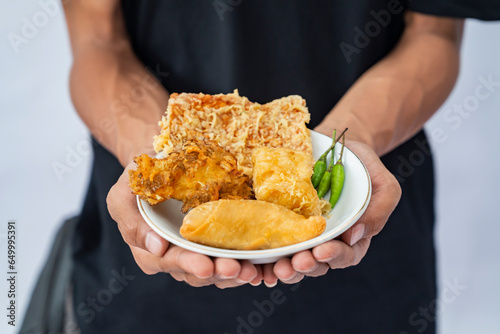 A human hand holding a plate with a gorengan