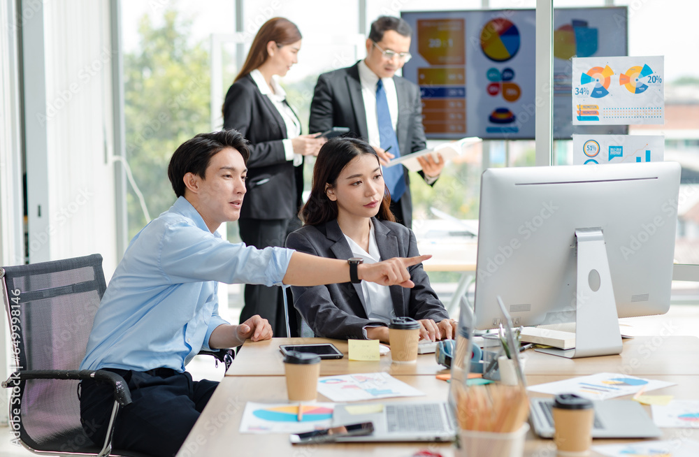 Fototapeta premium Asian professional successful male businessman mentor supervisor in casual outfit sitting smiling teaching helping female businesswoman intern colleague in formal suit working via computer in office.