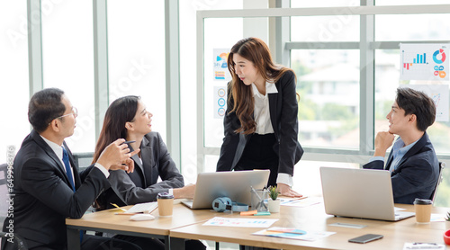 Asian professional successful businesswoman manager entrepreneur in formal suit standing teaching brainstorming marketing strategy with male female businessmen employees team in company meeting room